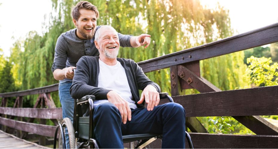 Trusted Assessor Assessing Telecare - man smiling pointing pushing wheel chair