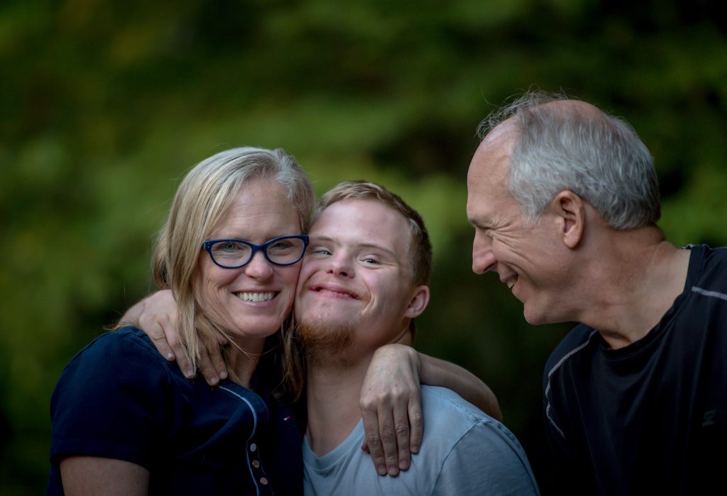 A woman, man and teenager with downs syndrome in the middle, all hugging