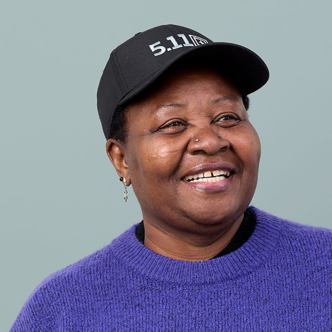 An image of a woman with dark skin wearing a fluffy purple jumper and a cap