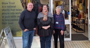 Photo of three people smiling stood outside of a charity shop