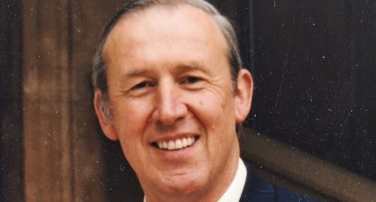 Photo of Tim Pape wearing a navy suit and tie.