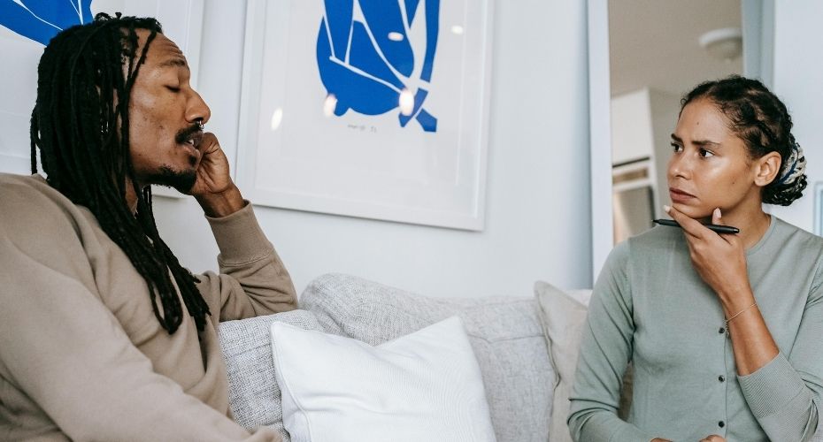 Man and woman speaking to each other, sitting on a sofa.