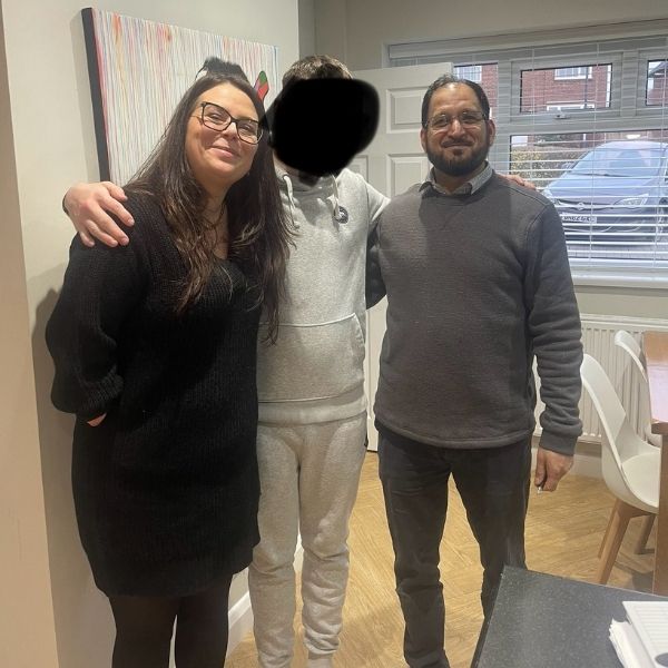 Photo of three people standing together smiling, with one face blurred out.