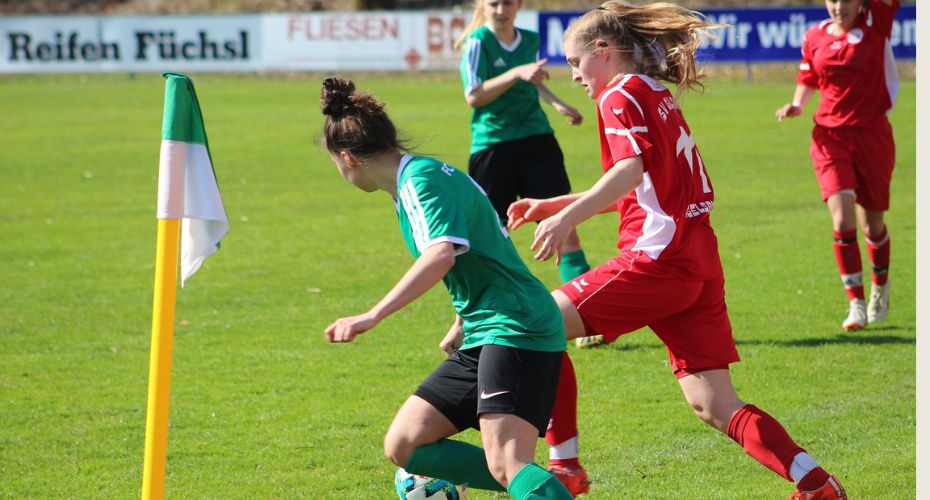 A woman in green and woman in red playing on the football pitch